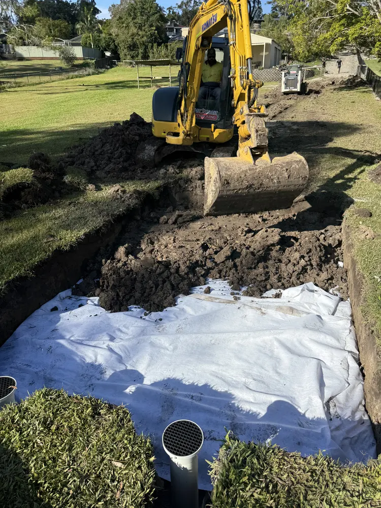 Excavator over the wide fabric-lined drainage trench at Oxenford