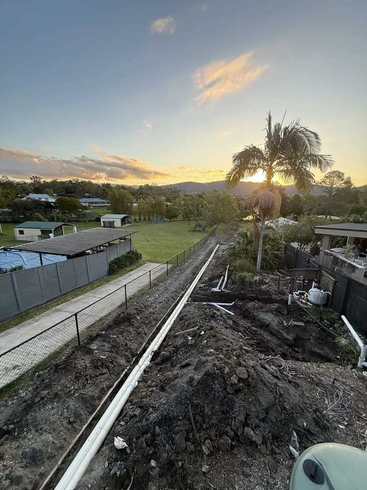 Backfilled drainage line running along the fence at dusk